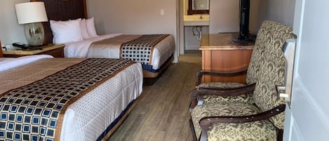Habitación de hotel con dos camas, un escritorio, una silla, una lámpara y un espejo.