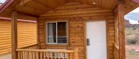 Una cabaña de madera con un porche, una ventana y una puerta.