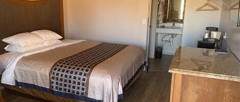Una cama bien hecha con una colcha estampada, un cabecero de madera y un aparador de madera con un espejo y una lámpara colgante.