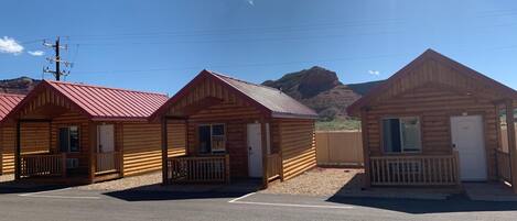 Three wooden cabins with red roofs, a gravel driveway, and a mountain in the background.