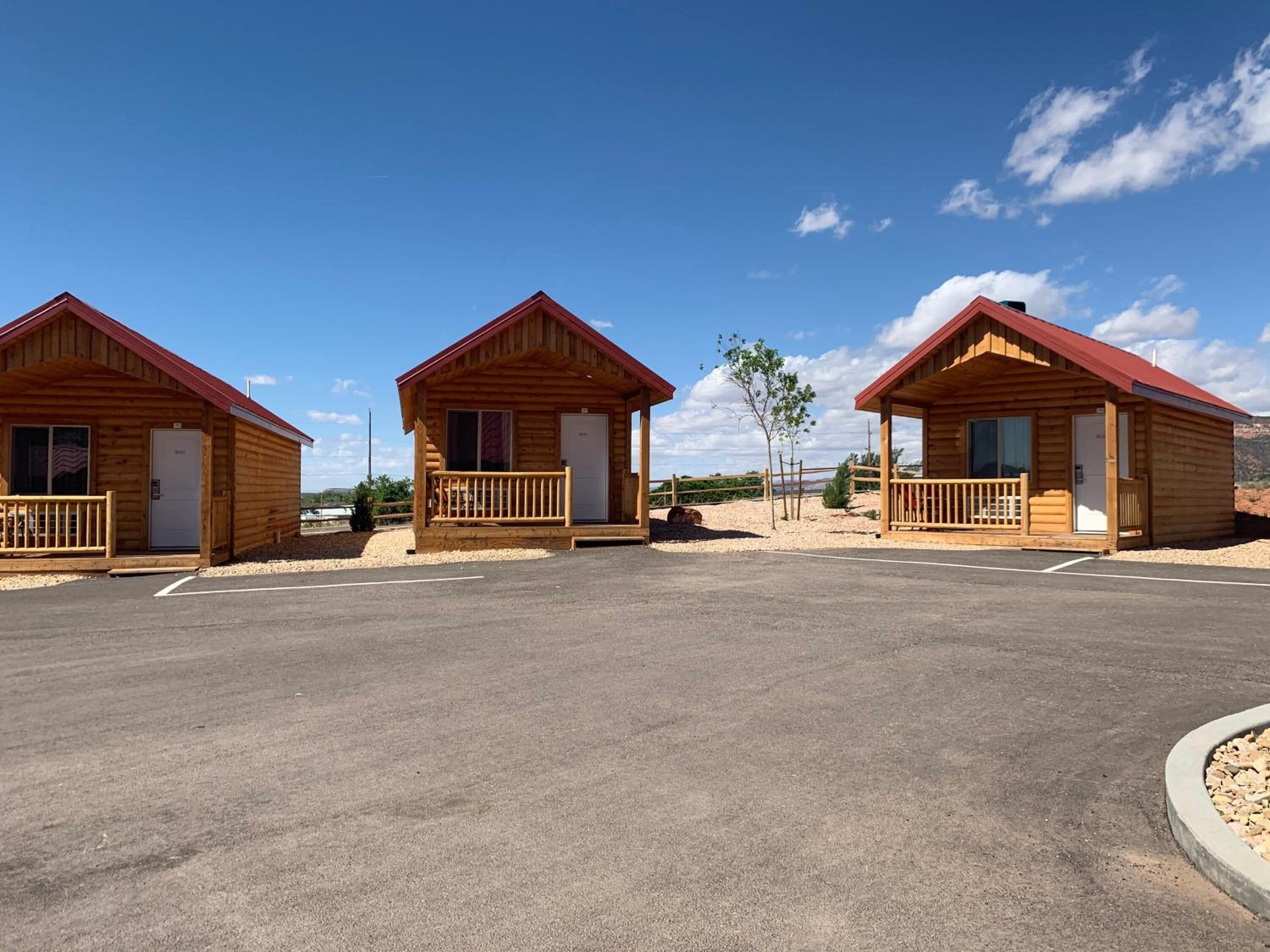 Three wooden cabins with red roofs, each featuring a porch and a door.