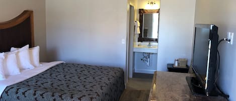 A hotel room with a bed, a wooden headboard, a TV, a bathroom with a sink and mirror, and a wooden ceiling.