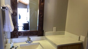 Une salle de bain avec un lavabo blanc, un miroir orné de motifs décoratifs en bois et un porte-serviettes.