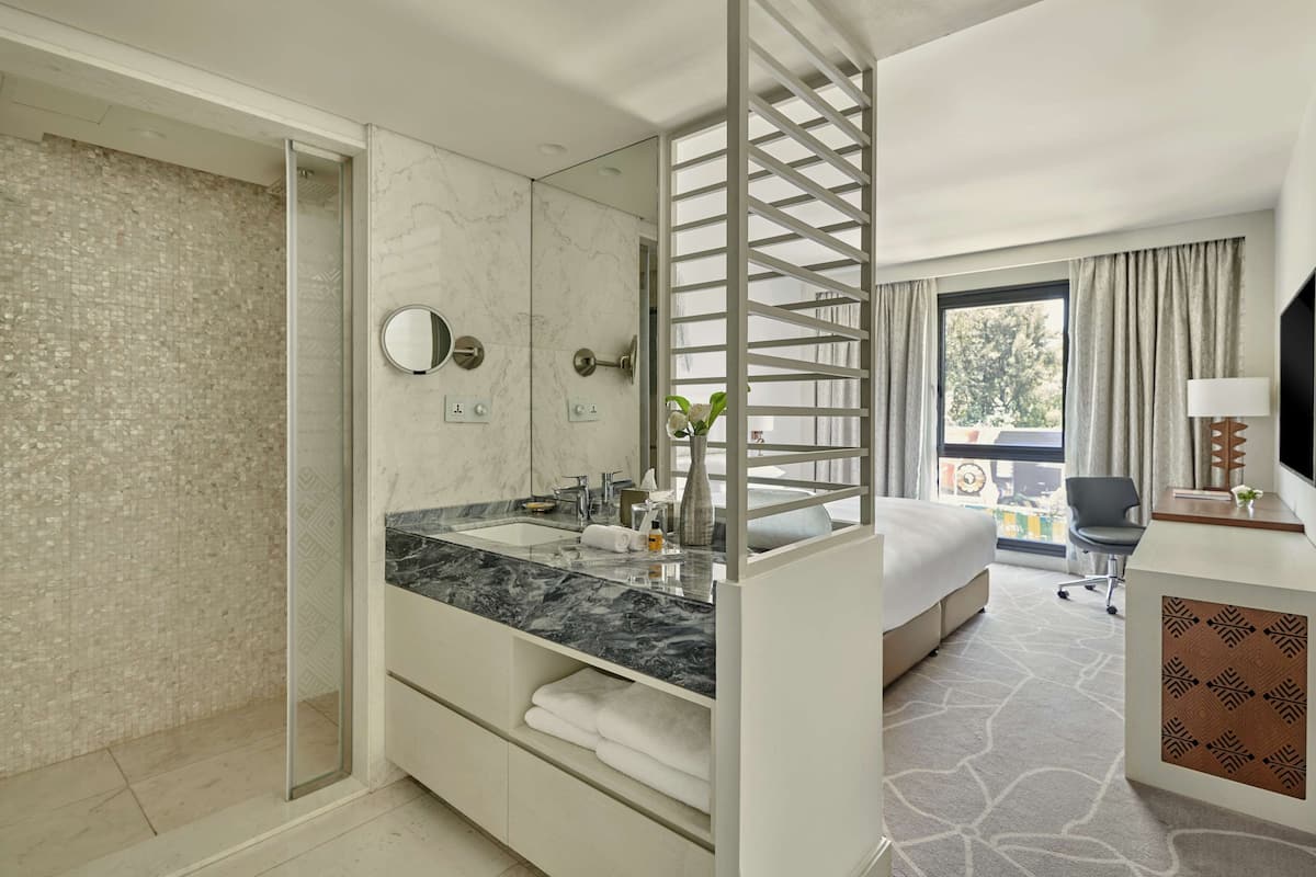 A modern hotel bathroom with a marble vanity, a large mirror, and a glass shower enclosure.
