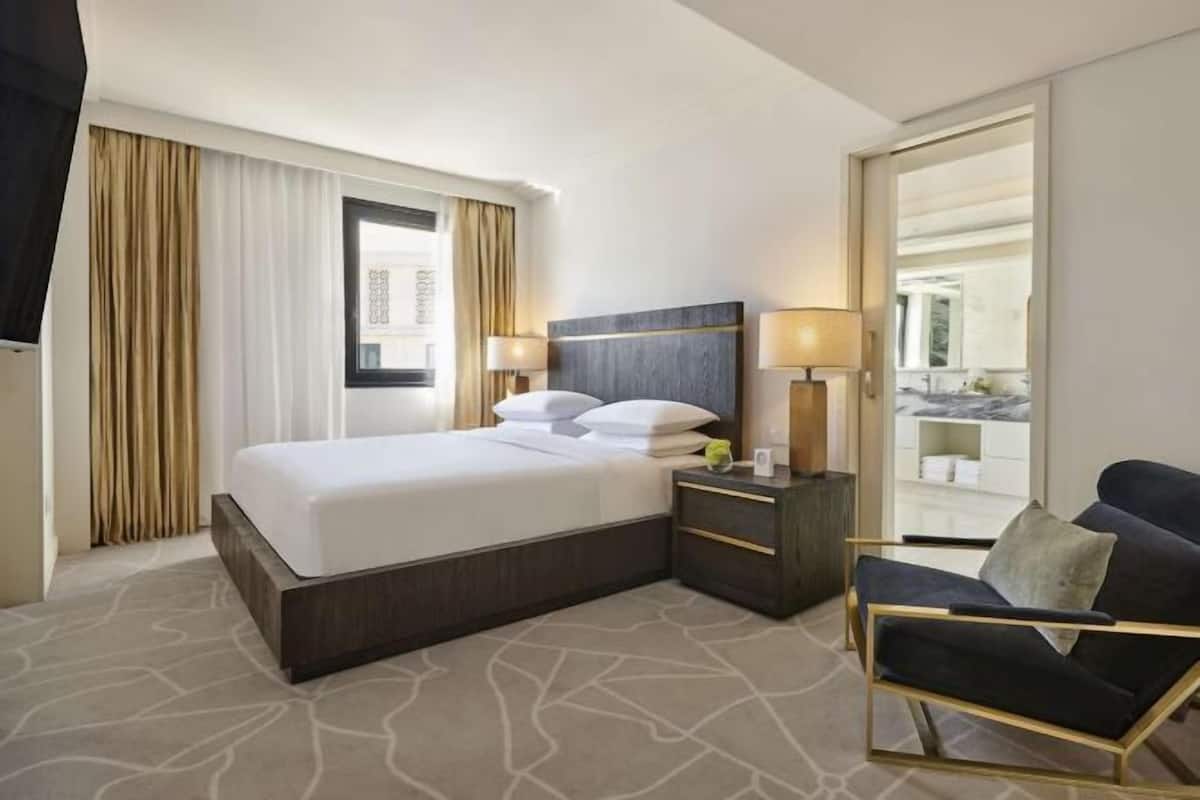 A hotel room with a bed, bedside tables, a chair, and a view through a window.