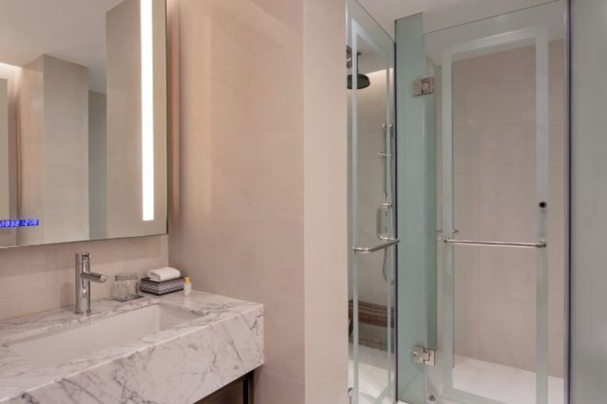 Un baño con lavamanos de mármol, cabina de ducha de vidrio y un espejo grande.