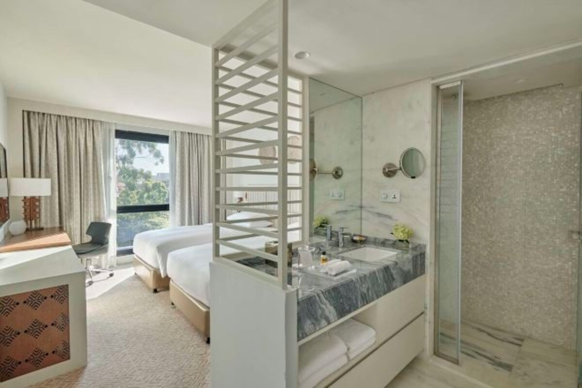 Una habitación de hotel con cama, escritorio, baño con ducha y un ventanal grande.