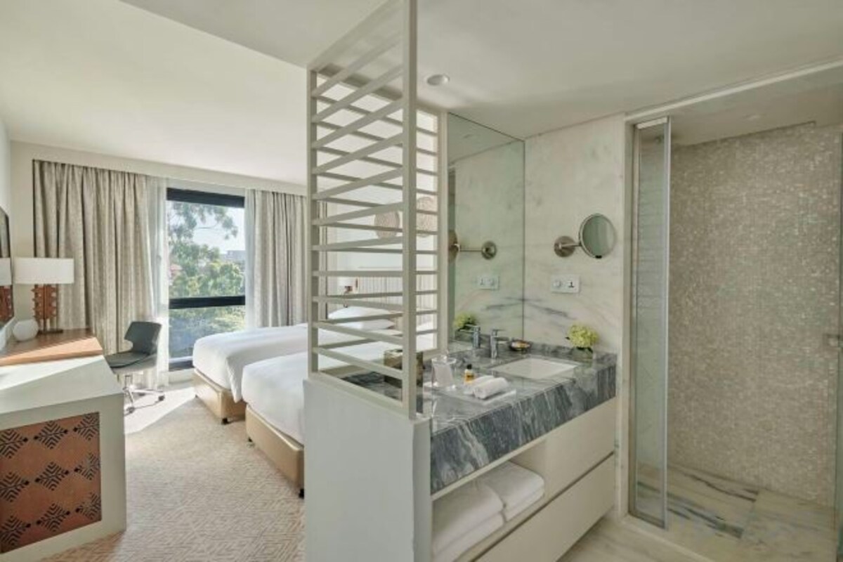 A modern hotel room with a bed, a bathroom with a shower, a large mirror, and a view of the outdoors.