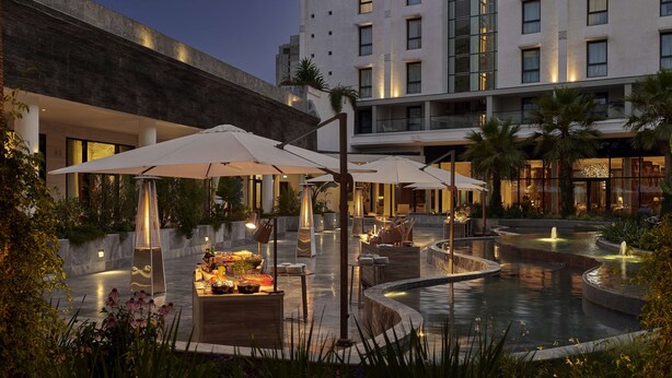 En moderne hotelgård med udendørs siddepladser, en pool og en hyggelig belysning.