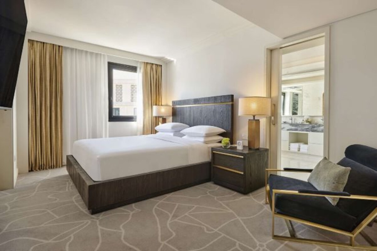 A hotel room with a bed, bedside tables, a chair, and a view through a window.