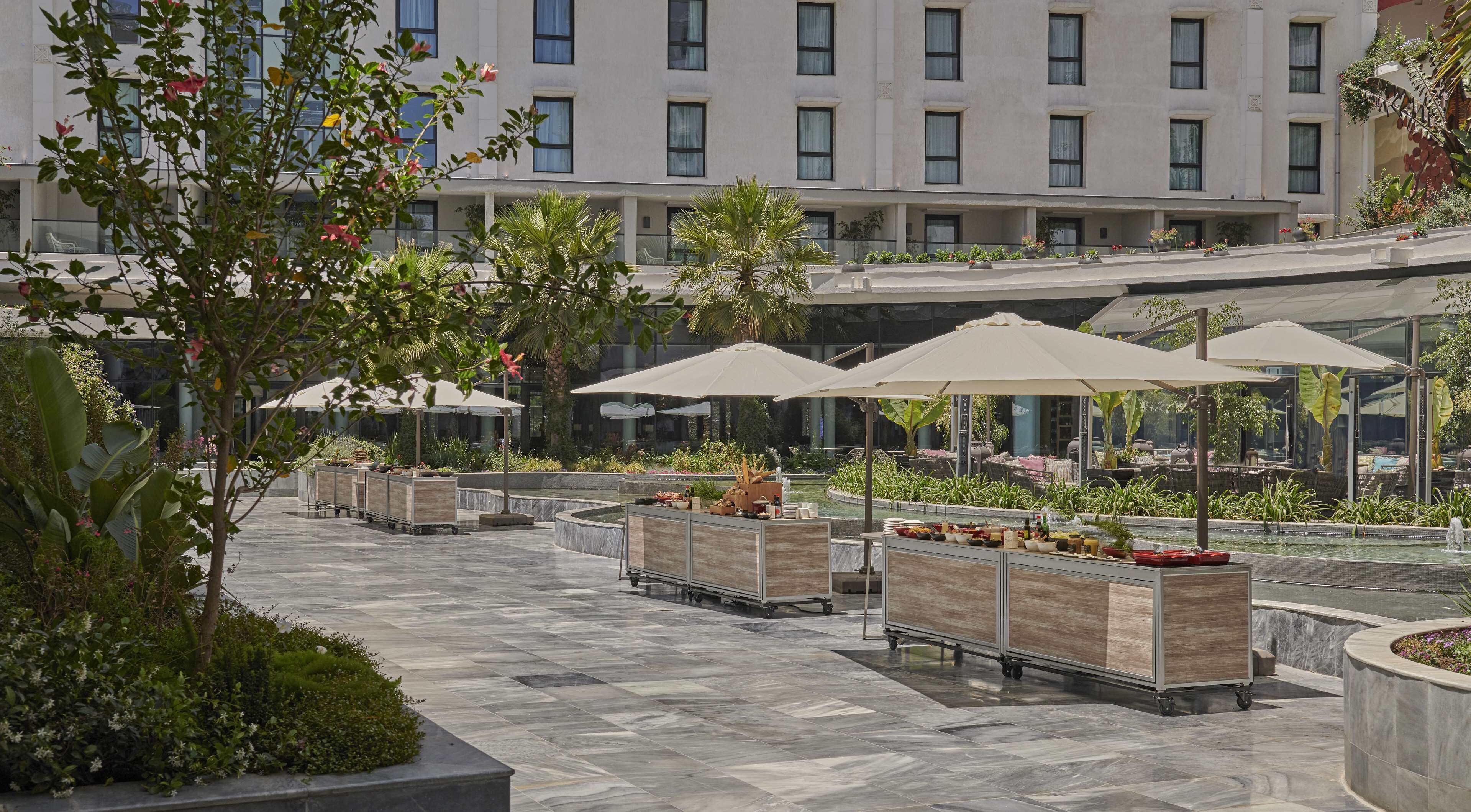 Une cour d’hôtel avec des espaces de détente en plein air, une fontaine ou un autre élément aquatique, et un bâtiment en arrière-plan.