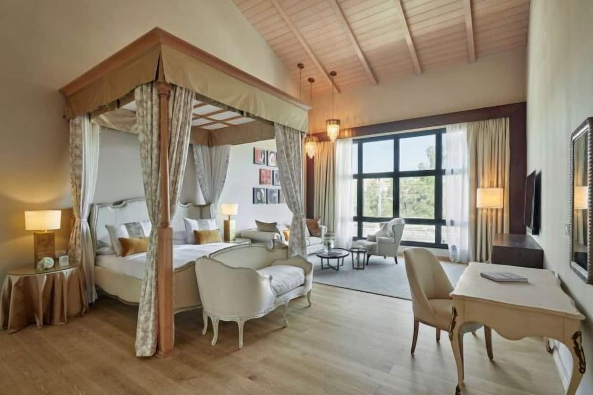 A bedroom with a canopy bed, a sitting area with a table and chairs, and a large window providing a view.