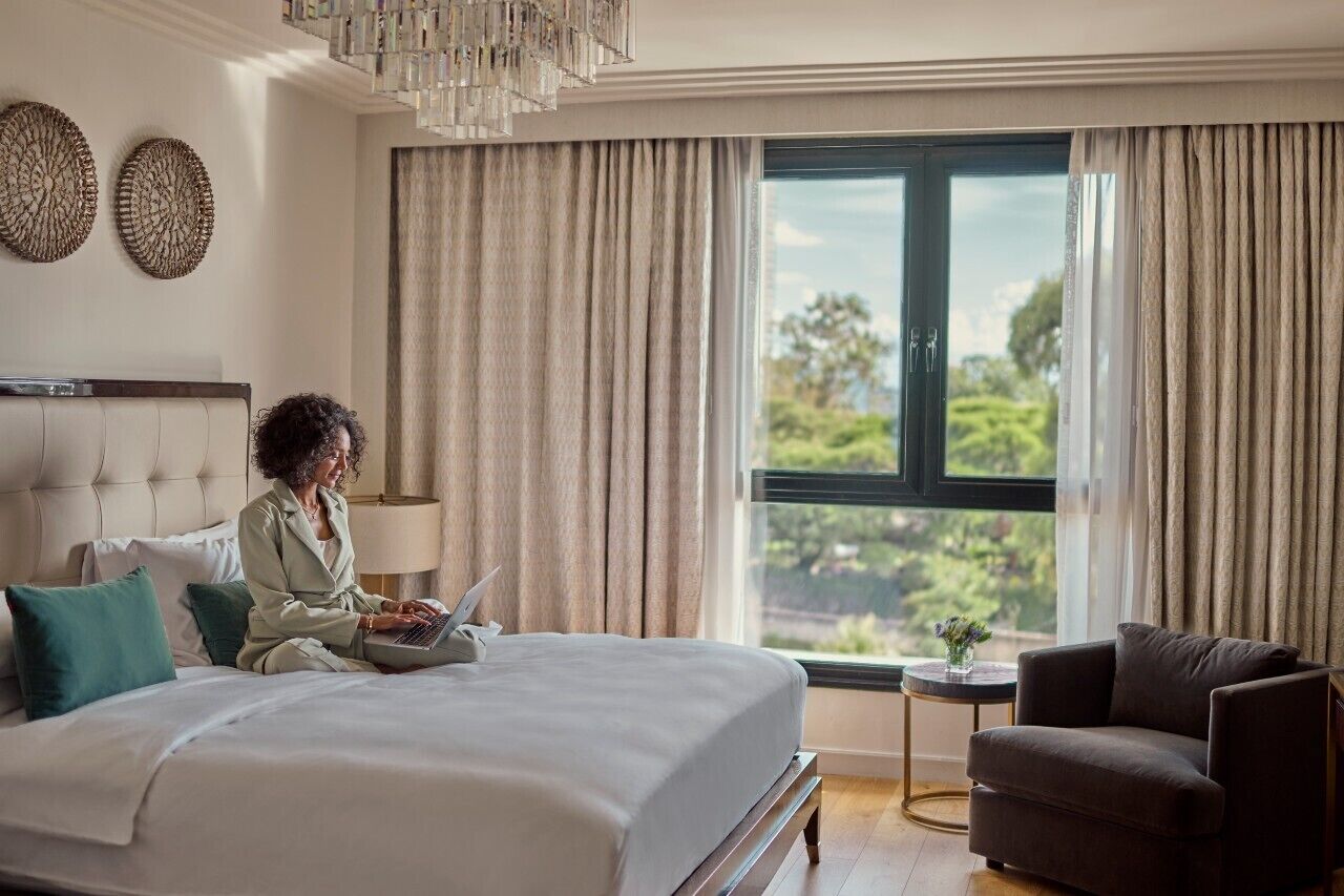 Une chambre d’hôtel avec un lit, un ordinateur portable, une chaise, une petite table avec un vase et des rideaux.