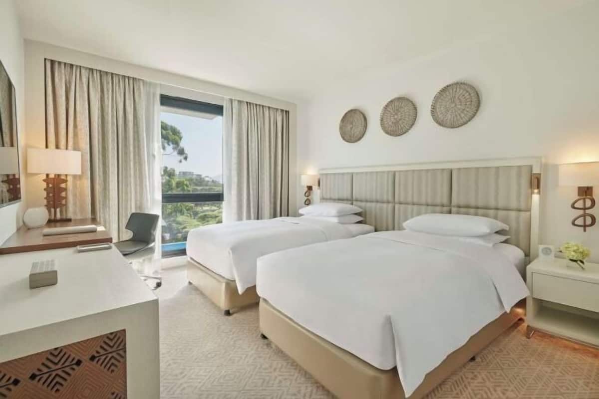 A hotel room with two beds, a desk, a chair, and a large window with curtains.