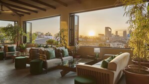 En moderne lounge med udsigt over byen, med en sofasæt, et sofabord i glas og plantekrukker.