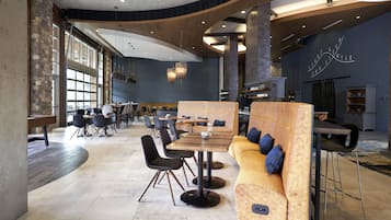 A spacious restaurant with high ceilings, large windows, and a mix of seating arrangements including tables and a long sofa.