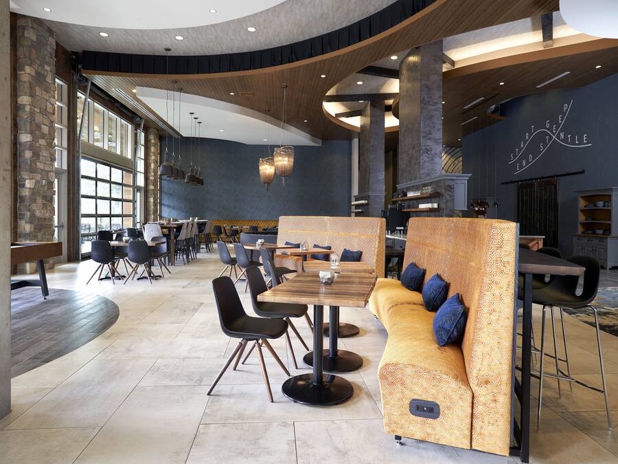 A spacious restaurant with high ceilings, large windows, and a mix of seating arrangements including tables and a long sofa.
