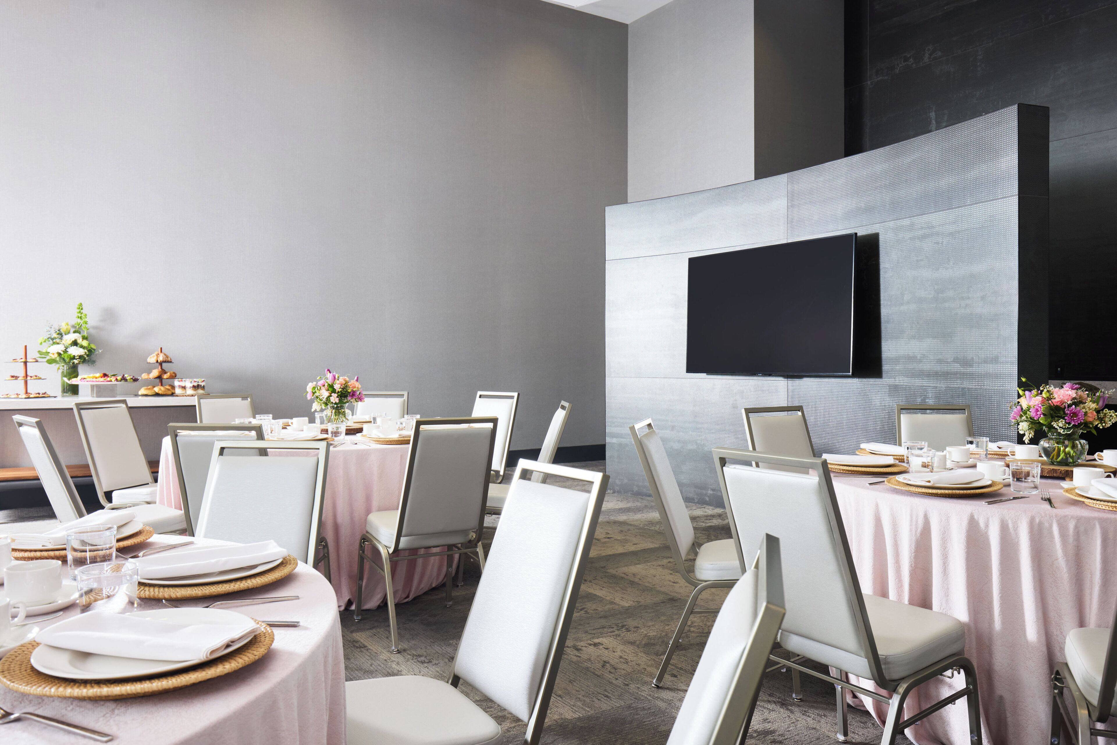 A conference room with round tables, white chairs, and a flat-screen TV mounted on the wall.