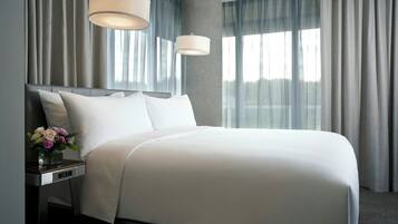 A modern hotel room with a large bed, a nightstand with a vase of flowers, and a large window with curtains.