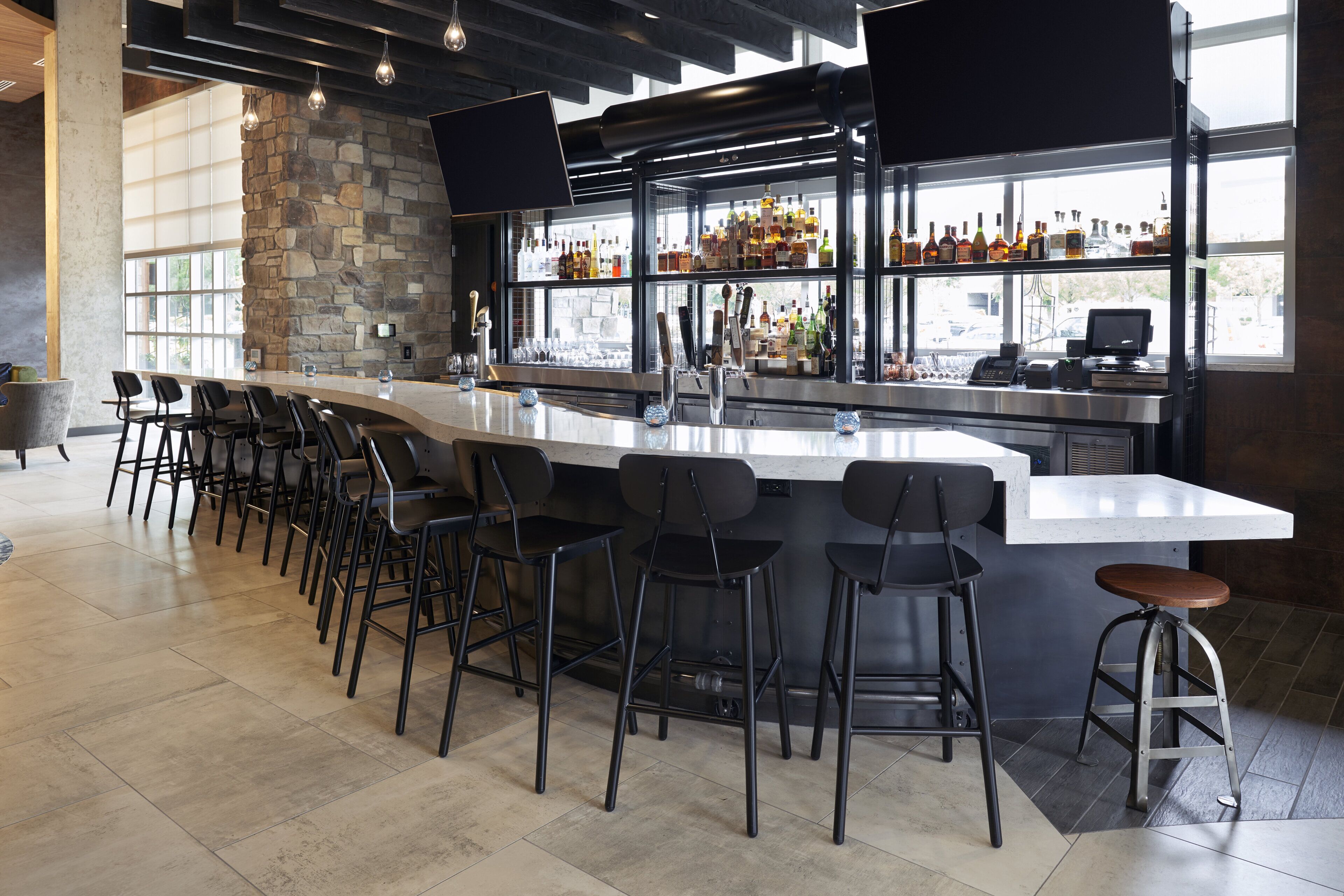 Un espace bar avec un mur en pierre, de nombreux tabourets, un comptoir et une variété de bouteilles.