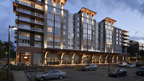 Un hôtel à plusieurs étages doté d’une architecture moderne, avec une entrée imposante et un parking pouvant accueillir plusieurs voitures.