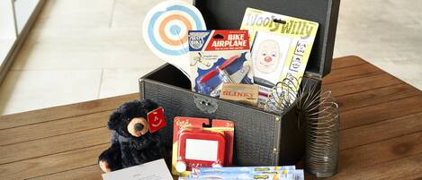 A wooden chest filled with children's toys and books, including a teddy bear, a toy airplane, and a box of gliders.