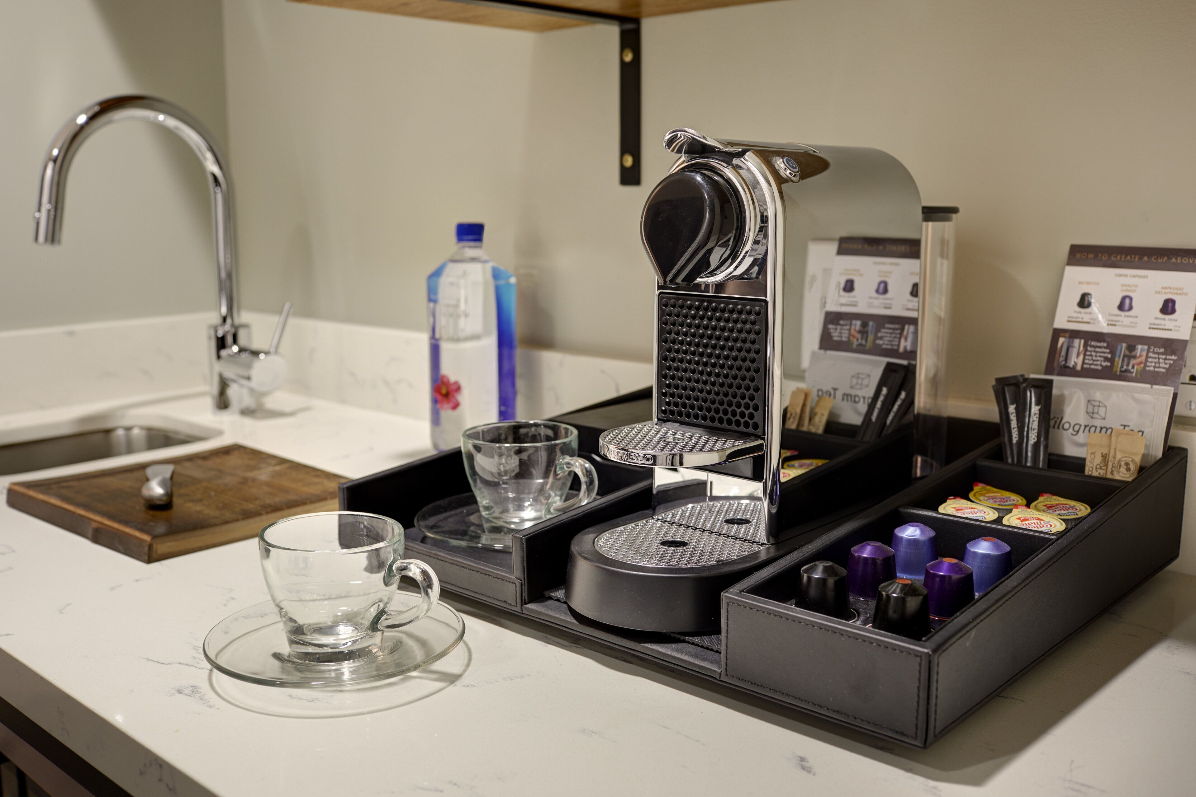 A coffee machine with a tray of cups and a water bottle on a kitchen counter.