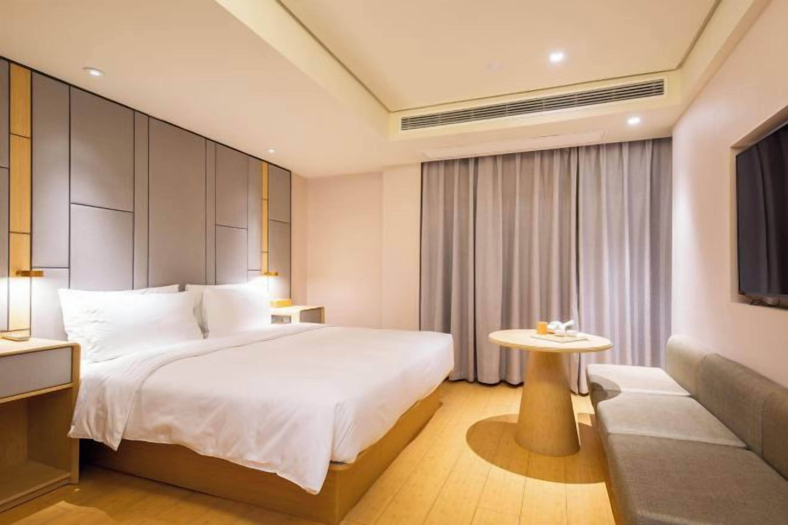 A modern hotel room with a large bed, bedside tables, a round table, and a sofa.