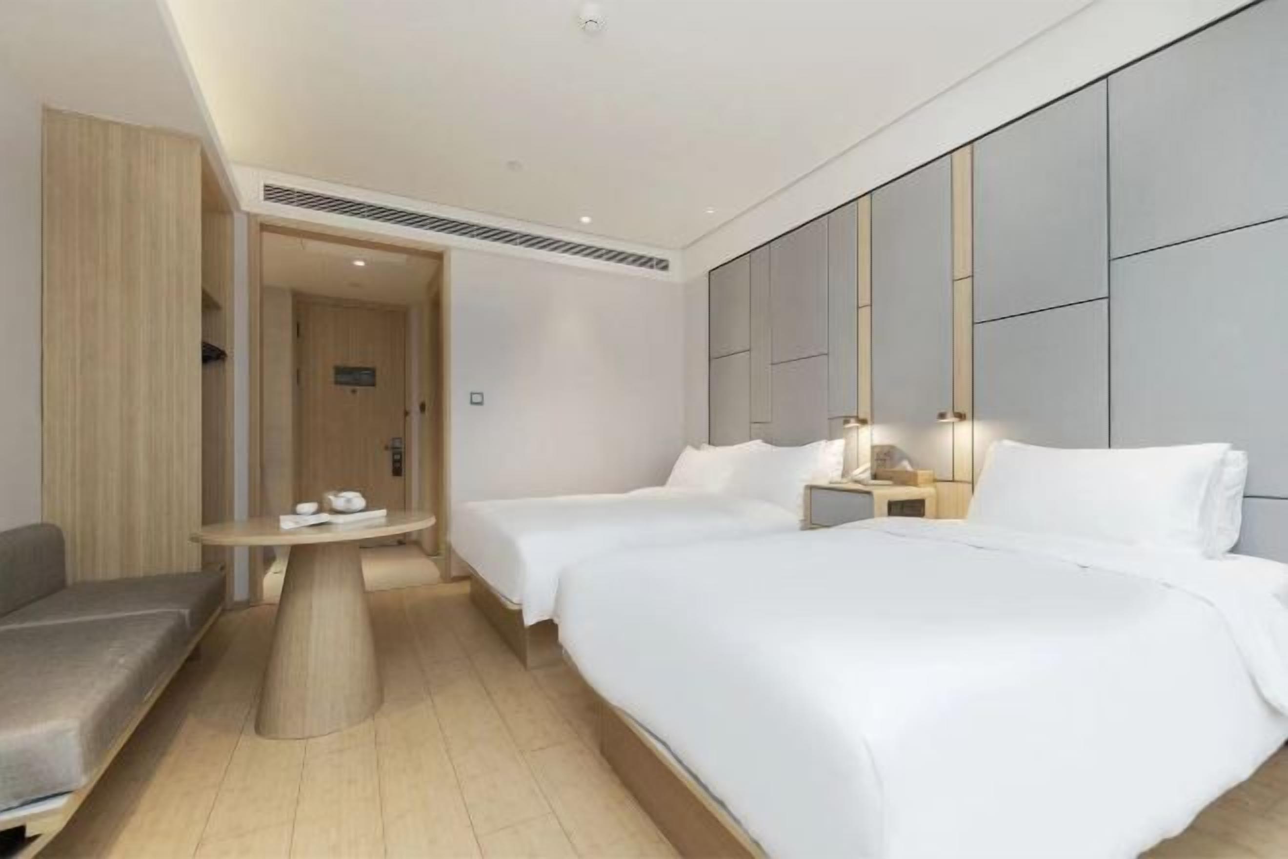 A hotel room with two beds, a sofa, a round table, and a small bedside table with a lamp.