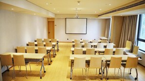 Een congreszaal met rijen tafels en stoelen, een projectiescherm en een groot raam met gordijnen.
