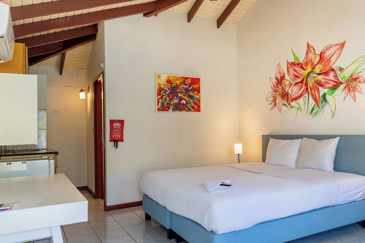 A hotel room with a bed, a desk, and a painting of flowers on the wall.