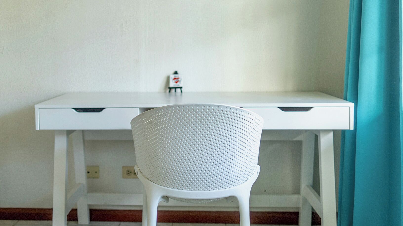 Un escritorio blanco con una silla perforada al frente.