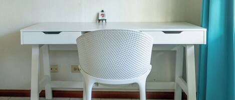 Un escritorio blanco con una silla perforada al frente.
