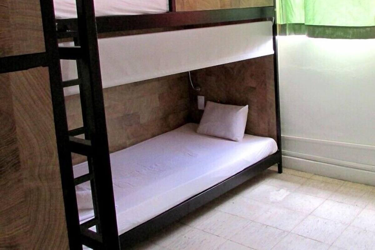 A bunk bed with a ladder, white bedding, and a green curtain in the background.