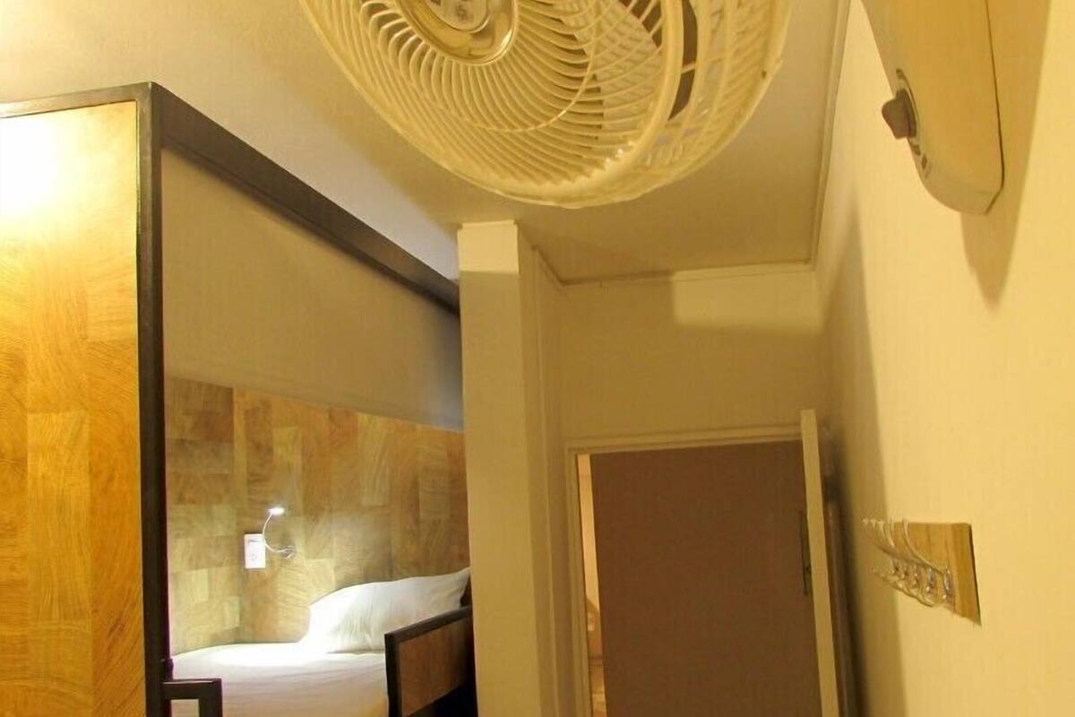 A room with a bed, a wooden headboard, a white wall, a door, and a ceiling fan.