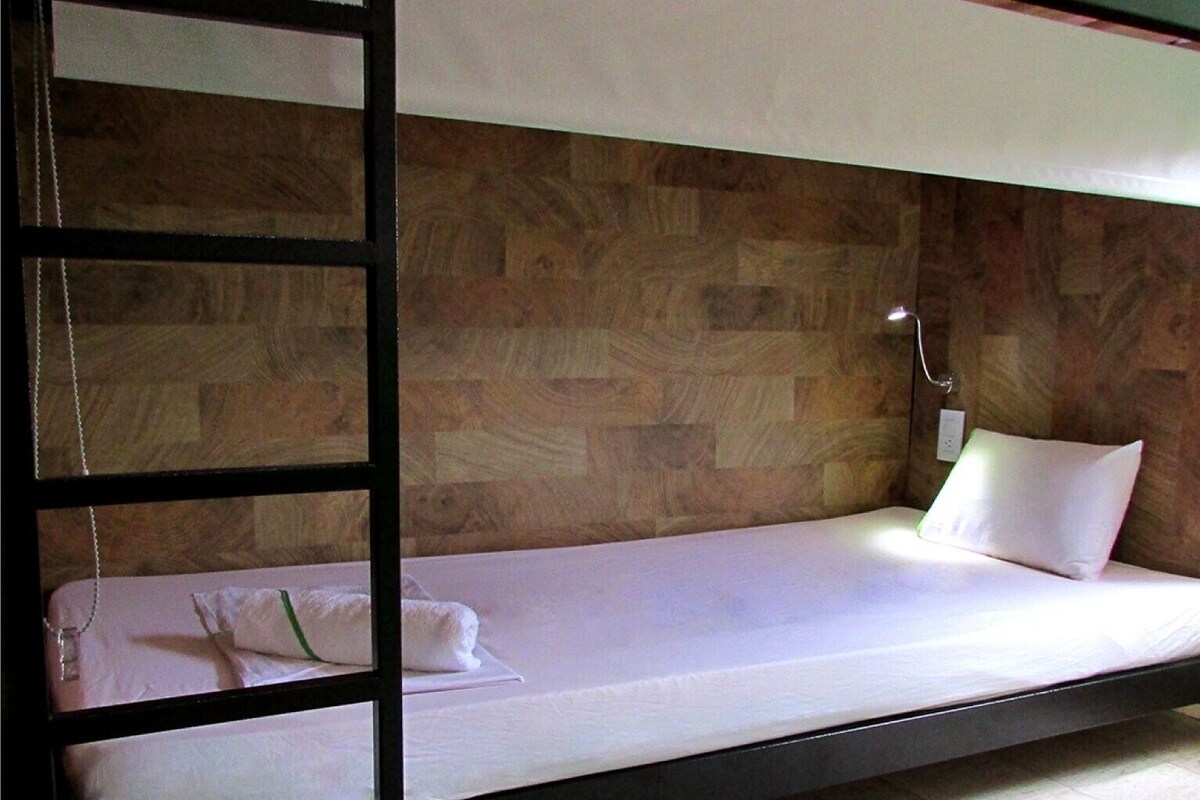 A bunk bed with a wooden headboard, a bedside table with a lamp, and a pillow on the lower bunk.