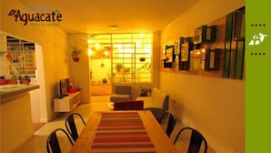 Un comedor con una mesa de madera y sillas, un tapete a rayas, y una zona de cocina con armarios y una ventana.