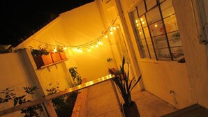 Un espacio al aire libre acogedor con un banco de madera, luces de cuerda y plantas en macetas.