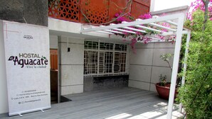 Un hostal llamado 'El Aguacate' con fachada blanca, un patio empedrado y una pérgola blanca adornada con flores rosas.