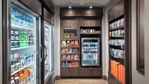 Un couloir équipé de distributeurs de boissons réfrigérées, d’étagères à collations et d’un présentoir à magazines.