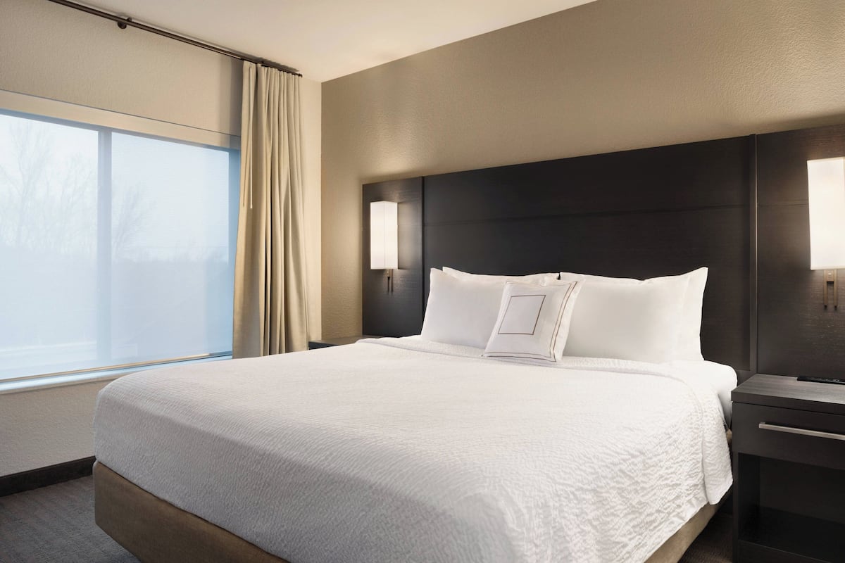 A hotel room with a large bed, a nightstand, a lamp, and a window with curtains.