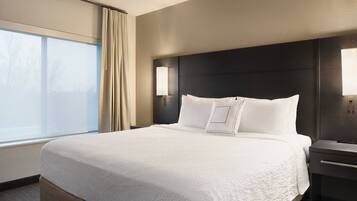 A hotel room with a large bed, a nightstand, a lamp, and a window with curtains.