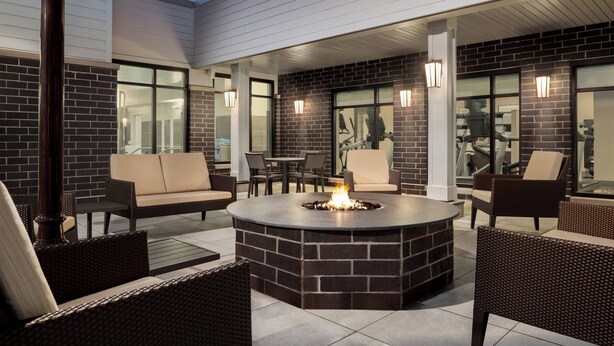 Un espace extérieur aménagé en patio, avec un foyer en briques, des meubles en osier et des portes vitrées donnant sur un espace intérieur.