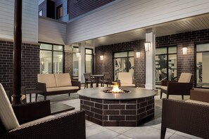 An outdoor patio area with a brick fire pit, wicker furniture, and glass doors leading to an interior space. - Residence Inn by Marriott Minneapolis St. Paul/Eagan (Eagan)
