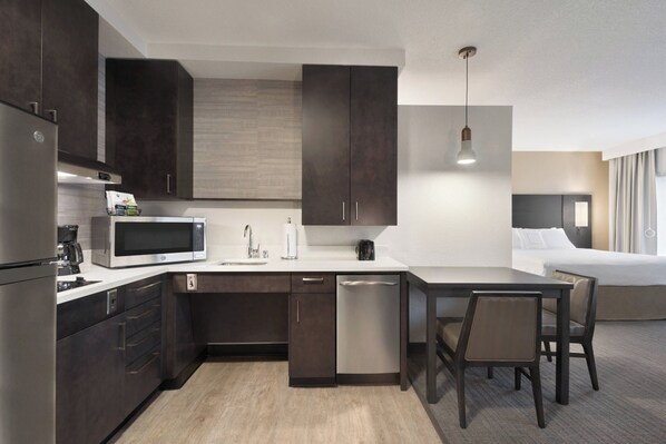 A compact hotel room with a kitchenette, a bed, and a dining area.
