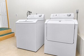 Two white front-loading washing machines in a room with a wooden door and a green carpeted staircase.