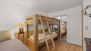 A room with a bunk bed, a desk with a lamp, and a door leading to another room.