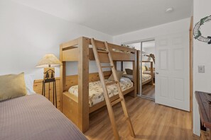 A room with a bunk bed, a desk with a lamp, and a door leading to another room.