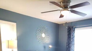 A bedroom with a bed, a ceiling fan, a decorative wall piece, a nightstand with a lamp, and a window with curtains. - Go Braves!- 3bd/2ba 6min from Mercedes-Benz/CNN/GWCC (Atlanta)