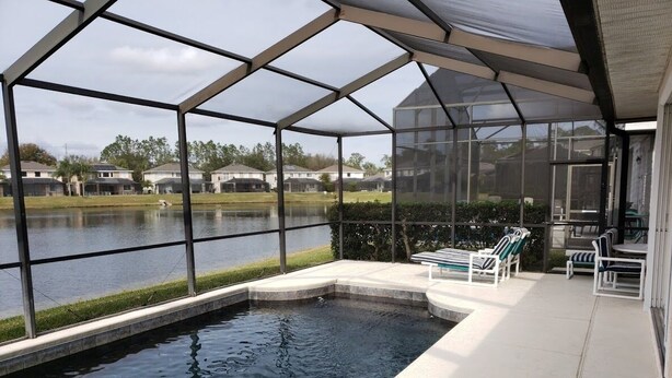 A swimming pool with a glass enclosure, a bench, and a table with chairs.
